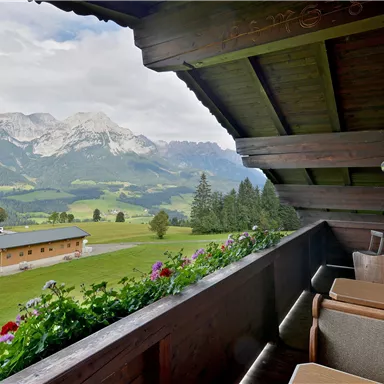 Ein gemütlicher Balkon mit Blick auf grüne Wiesen und beeindruckende Berge. Die natürliche Umgebung schafft eine entspannende Atmosphäre.