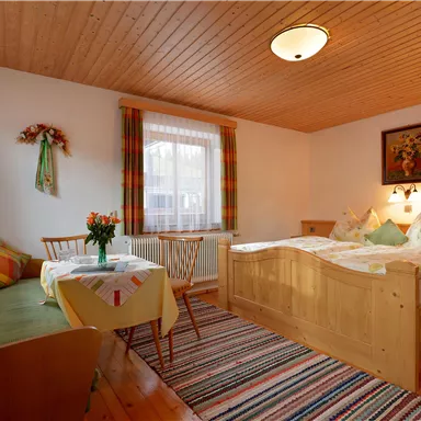 Ein gemütliches Zimmer mit einem Doppelbett und einer Sitzecke. Die Holzwände und farbenfrohen Vorhänge schaffen eine einladende Atmosphäre.