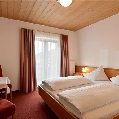 Ein gemütliches Hotelzimmer mit zwei Betten und einem Holzdecke. Ein kleiner Tisch und Stühle ergänzen die Einrichtung.