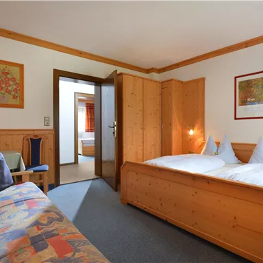 Ein gemütliches Zimmer mit Holzmöbeln und einem Doppelbett. Im Hintergrund ist ein weiterer Raum zu sehen.