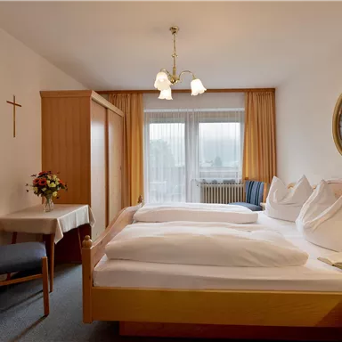 A cozy bedroom with two single beds and bright curtains. The room is inviting and has a small seating area with a table and chairs.