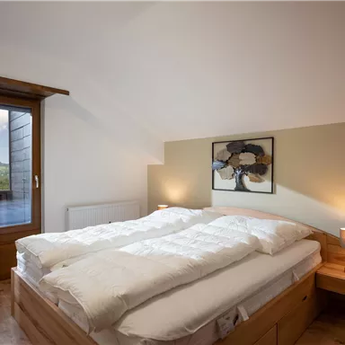 A cozy bedroom with a double bed and modern wooden design. The window offers a view of the mountains and provides plenty of daylight.