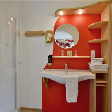 A modern bathroom with a shower and a sink. The walls are partially painted red and there are wooden shelves.