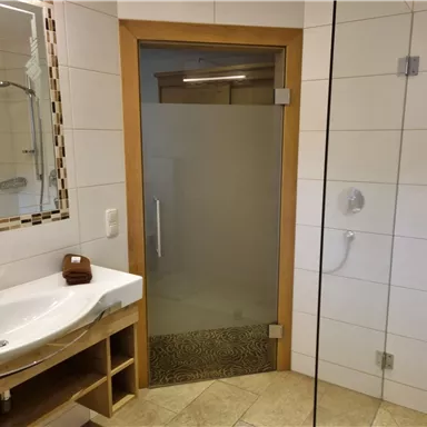 A modern bathroom with an elegant shower and a sink. The walls are tiled in light colors, and there is a large mirror.