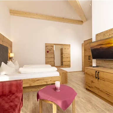 Ein modernes Zimmer mit Holzdetails und einem gemütlichen Bett. Der Raum verfügt über einen Fernseher, einen Tisch und eine rote Couch.