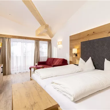 Ein modernes Hotelzimmer mit Holzinterieur und einem gemütlichen Doppelbett. Das Zimmer verfügt über eine Sitzecke, einen Fernseher und große Fenster mit Tageslicht.