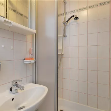A small bathroom with a shower and a sink. The walls are tiled and there is a mirror on the wall.