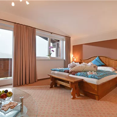 Ein gemütliches Schlafzimmer mit einem großen Doppelbett und einem Balkon. Der Raum ist hell und einladend, mit einem stilvollen Stuhl und einem Tisch mit frischen Früchten.