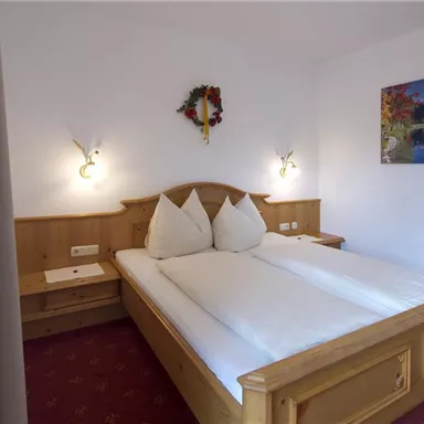 A cozy bedroom with two single beds and wooden paneling. A picture of a landscape hangs on the wall, and the room is decorated in warm colors.