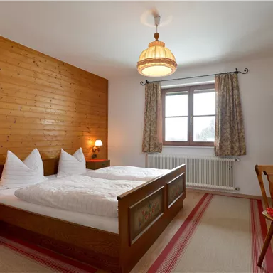 Ein gemütliches Schlafzimmer mit Holzverkleidung, zwei Betten und sanften Beleuchtung. Ein Fenster bietet Tageslicht und eine warme Atmosphäre.