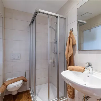 A modern bathroom with a shower, sink, and toilet. Light beige tiles and towels create a friendly atmosphere.