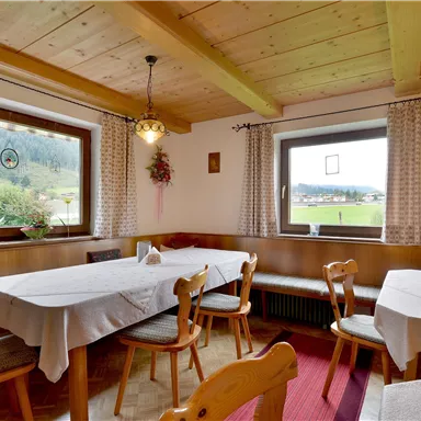 Ein gemütlicher Speisesaal mit Holz-Tisch und Stühlen. Der Raum ist hell erleuchtet und hat große Fenster mit Blick auf die Landschaft.