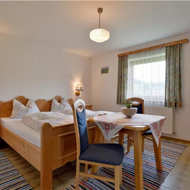 Ein gemütliches Schlafzimmer mit zwei Betten und einem Esstisch. Der Raum hat natürliche Holzoberflächen und wird von Tageslicht erhellt.