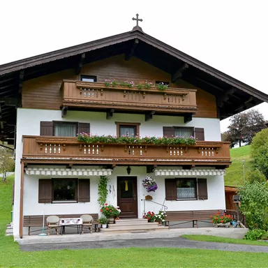 Ein schönes Holzhaus im alpinen Stil mit Balkonen und Blumen. Es steht in einer grünen Landschaft mit Bäumen im Hintergrund.