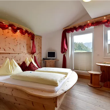 A cozy room with wooden paneling and large windows. There is a double bed, a small table, and a red armchair.