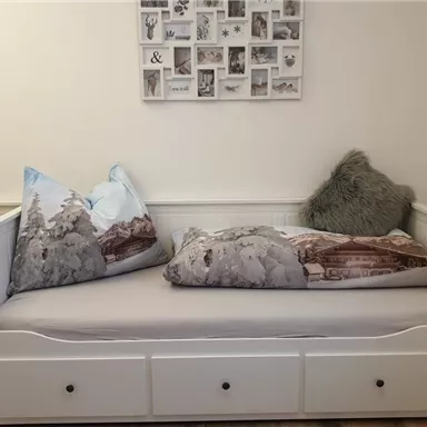 Ein gemütliches Tagesbett mit dekorativen Kissen. An der Wand hängt eine Bildercollage.