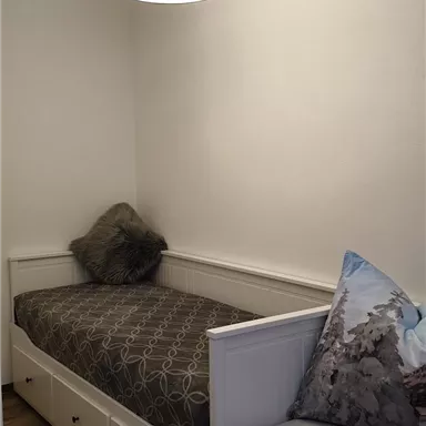 Ein gemütliches Zimmer mit einem Einzelbett und einem weiteren Sitzbereich. Die Wände sind hell und die Dekoration ist einfach und modern.