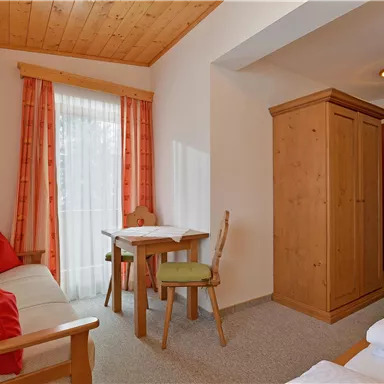 Ein gemütliches Wohnzimmer mit einem Sofa und einem Tisch. Es gibt große Fenster mit Vorhängen und einen Holzschrank.