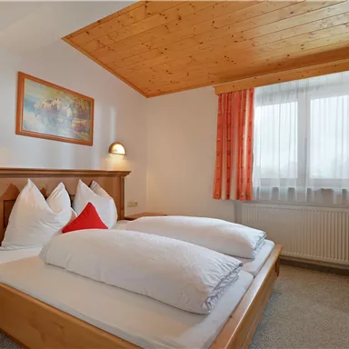 Ein gemütliches Schlafzimmer mit einem Doppelbett und zwei großen Kopfkissen. Das Zimmer ist hell dekoriert und hat große Fenster mit Aussicht.