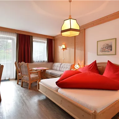 Ein gemütliches Hotelzimmer mit Holzverkleidung und roten Kissen. Es gibt einen kleinen Tisch, Stühle und einen Fernseher.