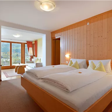 Ein gemütliches Zimmer mit einem Doppelbett und warmen Holzwänden. Das Fenster bietet einen Blick auf die Berge und viel natürliches Licht.