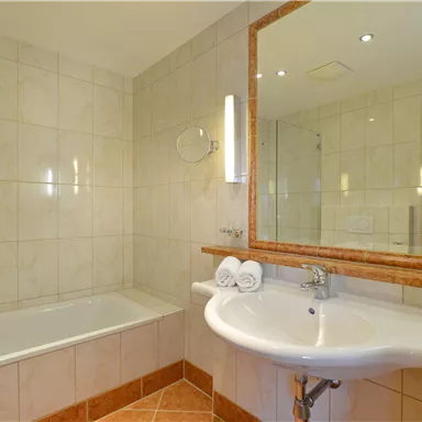 Ein modernes Badezimmer mit einer Badewanne und einer Dusche. Der Waschbeckenbereich ist hell und gut beleuchtet, mit einem großen Spiegel.