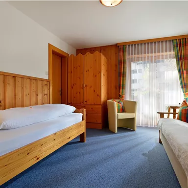 Ein gemütliches Zimmer mit Holzmöbeln und Teppichboden. Die Fenster sind hell und lassen viel Licht herein.