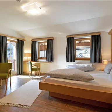 Ein modernes Schlafzimmer mit Holzdekor und großen Fenstern. Es gibt ein Doppelbett, einen Fernseher und gemütliche Sitzgelegenheiten.