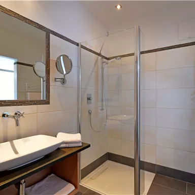 Ein modernes Badezimmer mit einer Dusche und einem eleganten Waschbecken. Helle Fliesen und ein großer Spiegel sorgen für ein frisches Ambiente.