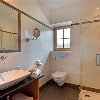 Ein modernes Badezimmer mit einer Dusche und einem großen Spiegel. Die sanitären Anlagen sind in neutralen Farben gehalten und wirken sauber und einladend.