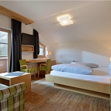 Ein gemütliches Zimmer mit Holzdekor und einer großen Fensterfront. Es gibt ein Doppelbett, einen kleinen Tisch und zwei Stühle.