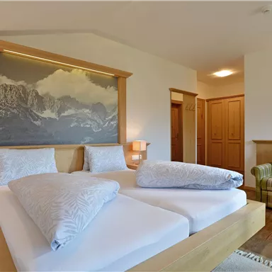 Ein gemütliches Schlafzimmer mit zwei Betten und einer Holzmöbelgestaltung. Im Hintergrund ist ein Wandbild mit Bergmotiven zu sehen.