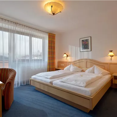 Ein helles Schlafzimmer mit zwei Einzelbetten und einer gemütlichen Sitzecke. Große Fenster sorgen für viel Tageslicht.