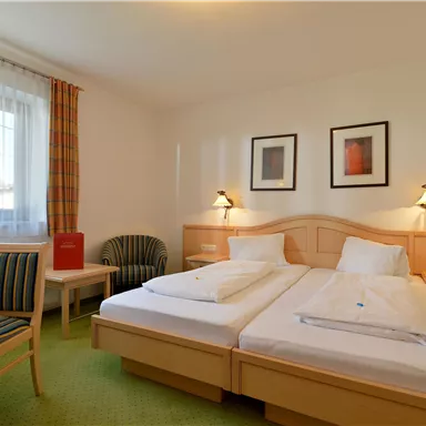 Ein gemütliches Hotelzimmer mit zwei Einzelbetten und einem kleinen Tisch. Es gibt einen Stuhl und Dekoration an den Wänden.