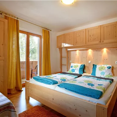 Ein gemütliches Schlafzimmer mit einem Doppelbett und Holzregalen. Große Fenster mit Vorhängen sorgen für viel Licht.