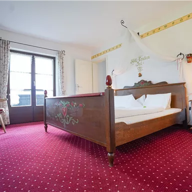 Ein gemütliches Schlafzimmer mit einem großen Bett und traditionellen Möbeln. Der Raum hat einen roten Teppich und Fenster mit Blick nach draußen.