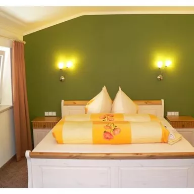 Ein gemütliches Schlafzimmer mit einem großen Bett und gelben Kissen. Die Wände sind grün gestrichen und es gibt Fenster mit Vorhängen.