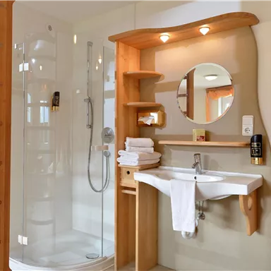 A modern bathroom with a shower and a sink. Wooden shelves and towels give the room a cozy atmosphere.