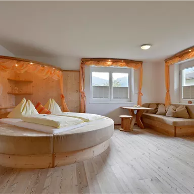 A cozy room with a round bed construction and light wood. The windows are large, providing plenty of light, and the pleasant ambiance is emphasized by the soft curtains.