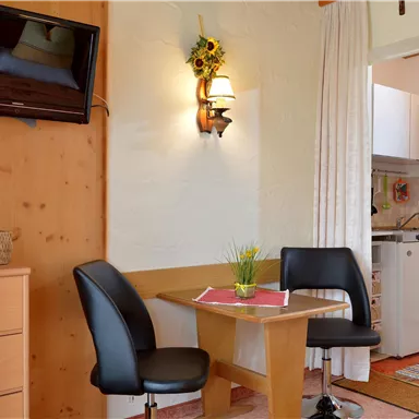 Ein gemütlicher Essbereich mit einem Tisch und zwei Stühlen. Im Hintergrund ist die Küche sichtbar, und an der Wand hängt ein Fernseher.