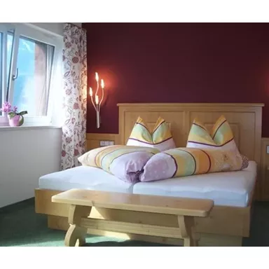 Ein gemütliches Schlafzimmer mit einem großen Bett und bunten Kissen. Die Wände sind in warmen Farben gestaltet und es gibt einen schönen Blick aus dem Fenster.