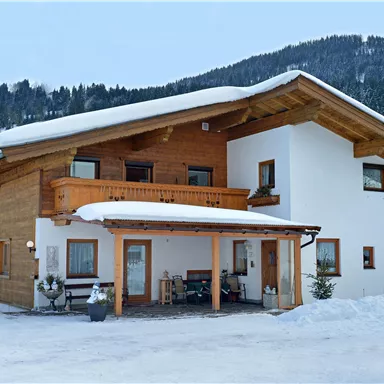 A modern house with a wood and plaster façade in a snowy landscape. Mountains are visible in the background.