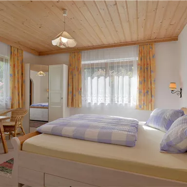 Ein gemütliches Schlafzimmer mit Holzdecken und großen Fenstern. Das Zimmer verfügt über ein Doppelbett und einen Tisch mit Stühlen.