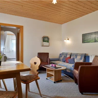 Ein gemütliches Wohnzimmer mit einem Sofa und zwei Sesseln. Ein Tisch steht in der Mitte, und es gibt eine Tür zu einem anderen Raum.