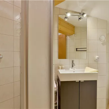 Ein modernes Badezimmer mit einer Dusche, einem Waschbecken und einer Toilette. Die Wände sind gefliest und die Einrichtung ist hell und funktional.