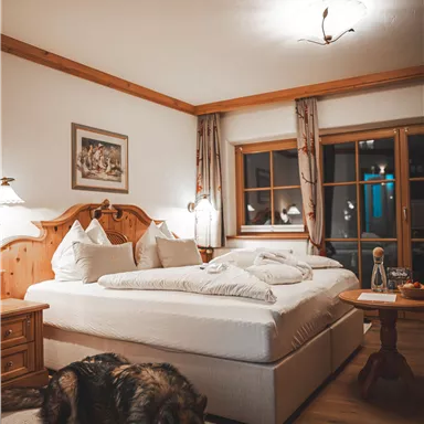 Ein gemütliches Schlafzimmer mit einem großen Bett und warmem Holzdekor. Ein Hund liegt entspannt auf einem Teppich neben dem Bett.