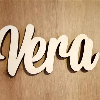 A wooden sign with the name "Vera" in cursive writing. The background is a light wood surface.