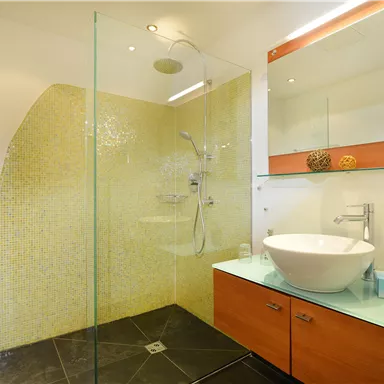 Ein modernes Badezimmer mit einer Glasdusche und einem eleganten Waschbecken. Die Wände sind mit bunten Fliesen dekoriert, und es gibt einen praktischen Handtuchhalter.