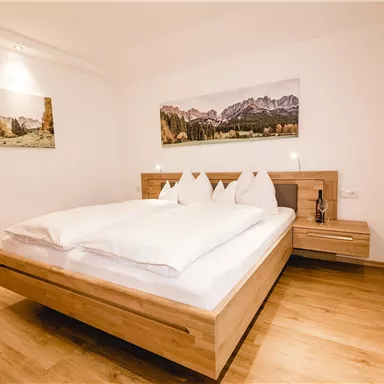 Ein modernes Schlafzimmer mit einem großen Bett und Holzdetails. An der Wand hängen Bilder von Bergen, und der Raum ist hell und einladend.