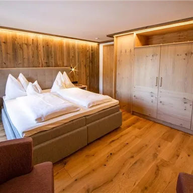 A modern bedroom with a large bed and wood paneling. Cozy furniture and warm lighting create an inviting atmosphere.